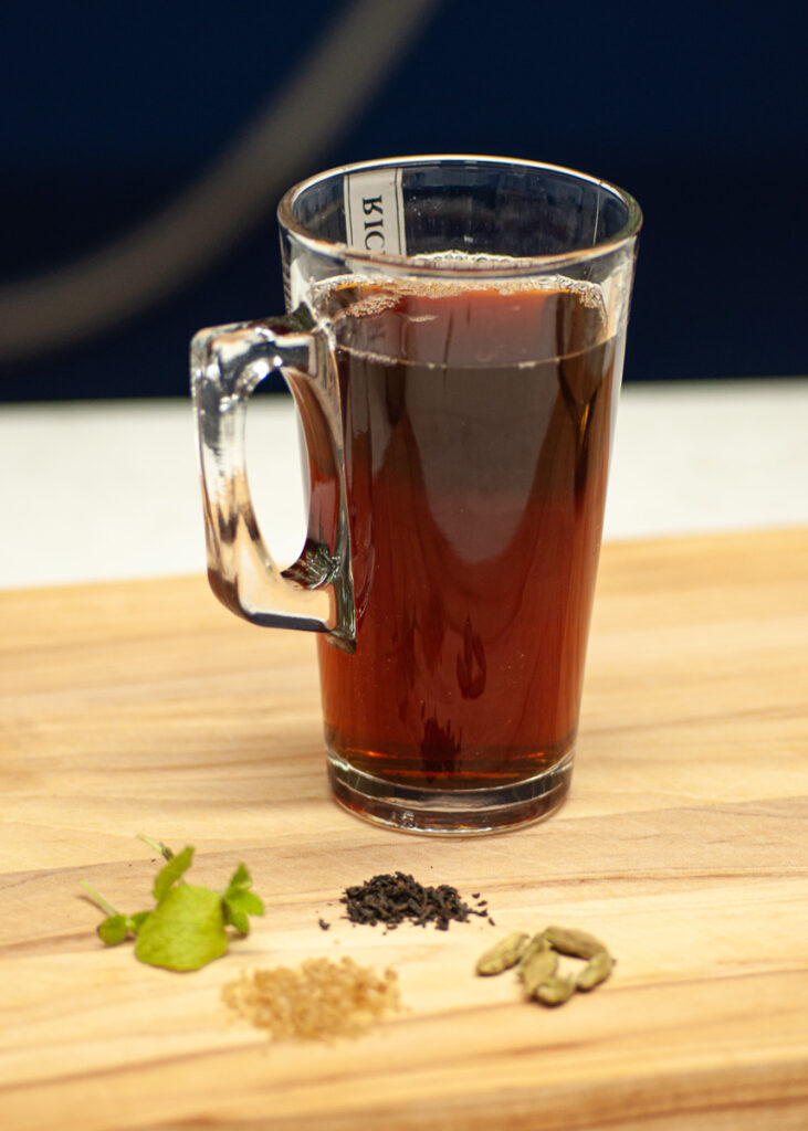 zimowa herbata w szklance z rozłożonymi obok składnikami - mięta, kardamonem, herbatą i cukrem